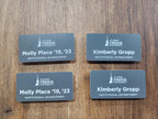 Custom engraved name tags with St. John Fisher University logo on wood surface