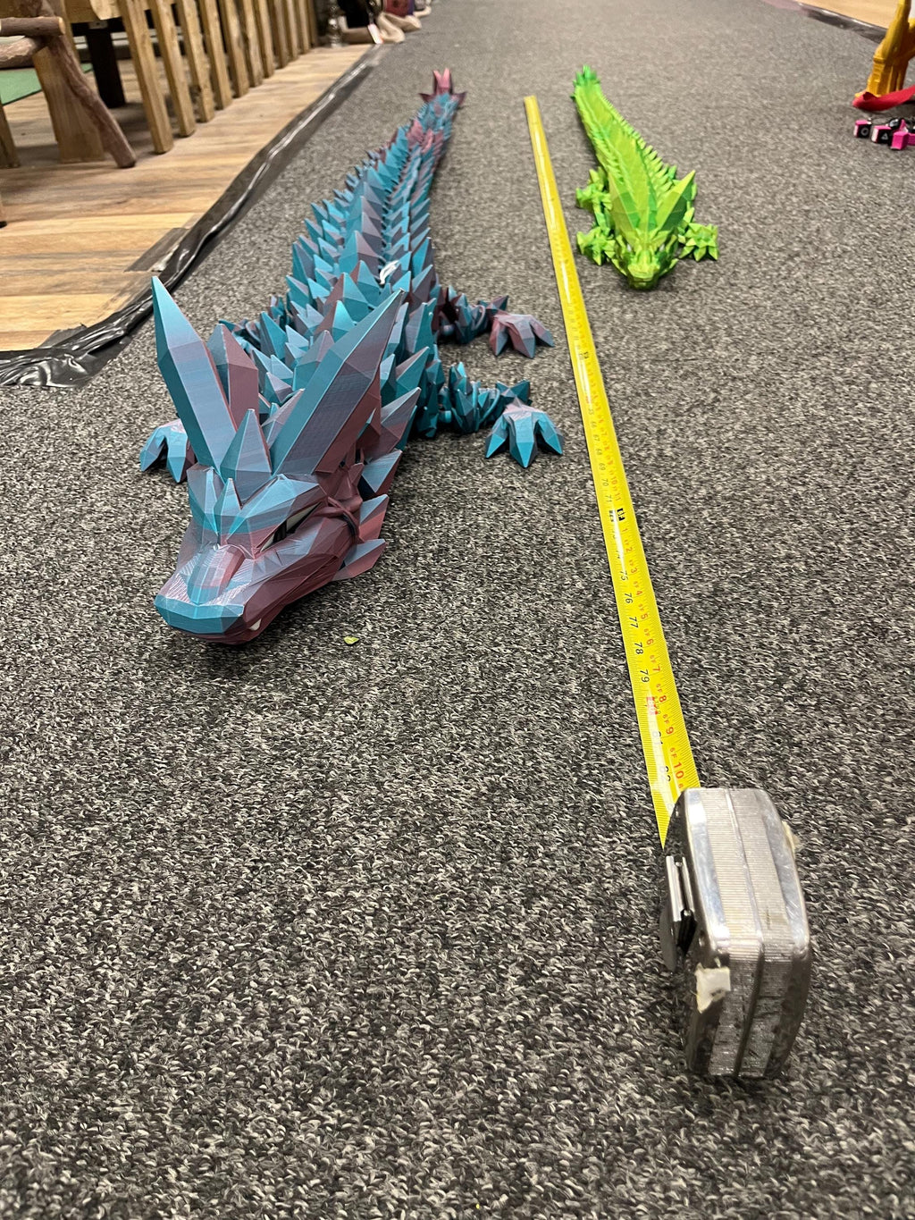 Large low-poly 3D printed dragon and smaller green dragon beside measuring tape on carpet