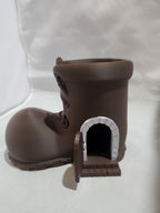 3D printed brown boot-shaped house with a small open door and white brick archway