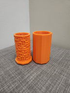 Two orange 3D printed cylindrical containers, one with a maze pattern, on a gray fabric surface.