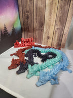 Four colorful 3D printed dragon figurines on display with a wood and aurora background.