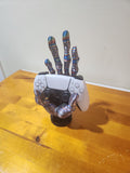 3D printed multicolor hand-shaped holder displaying a white gaming controller on a wooden table