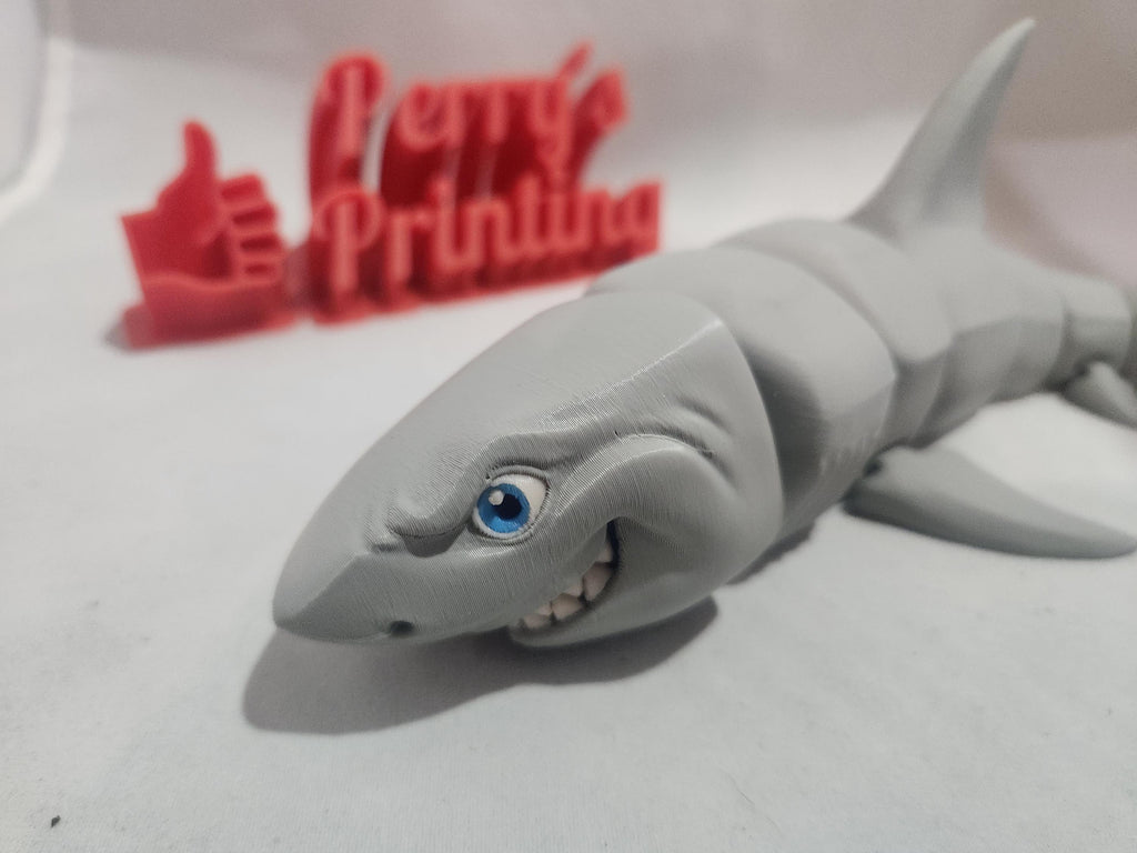 3D printed smiling shark figurine with detailed face and flexible segmented body, on white background.