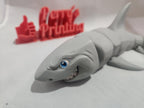 3D printed smiling shark figurine with detailed face and flexible segmented body, on white background.
