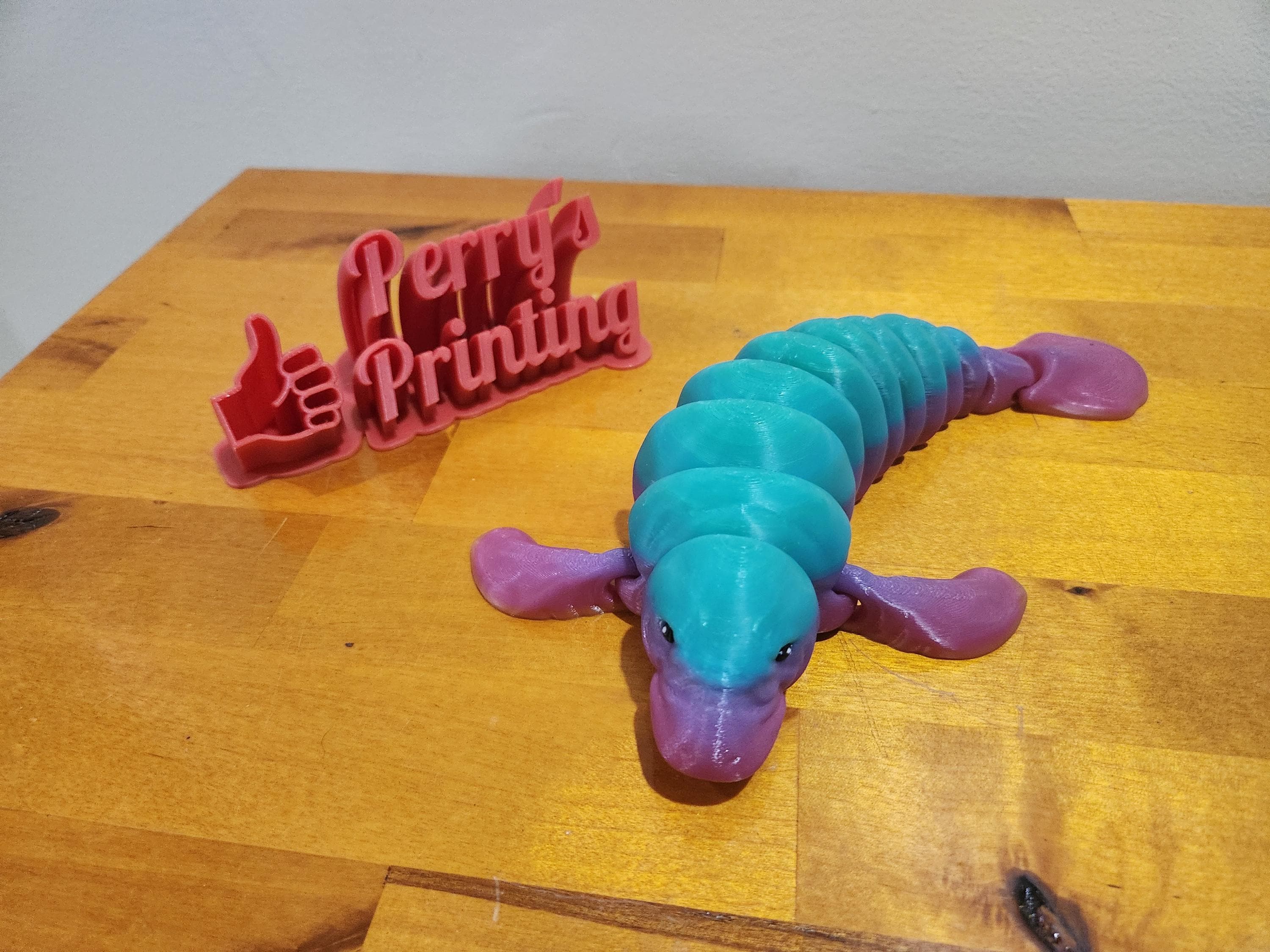 3D printed blue and purple articulated axolotl and red Perry's Printing sign on wooden table