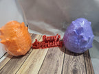 3D printed orange and purple dragon eggs with Perry's Printing sign on wood surface.