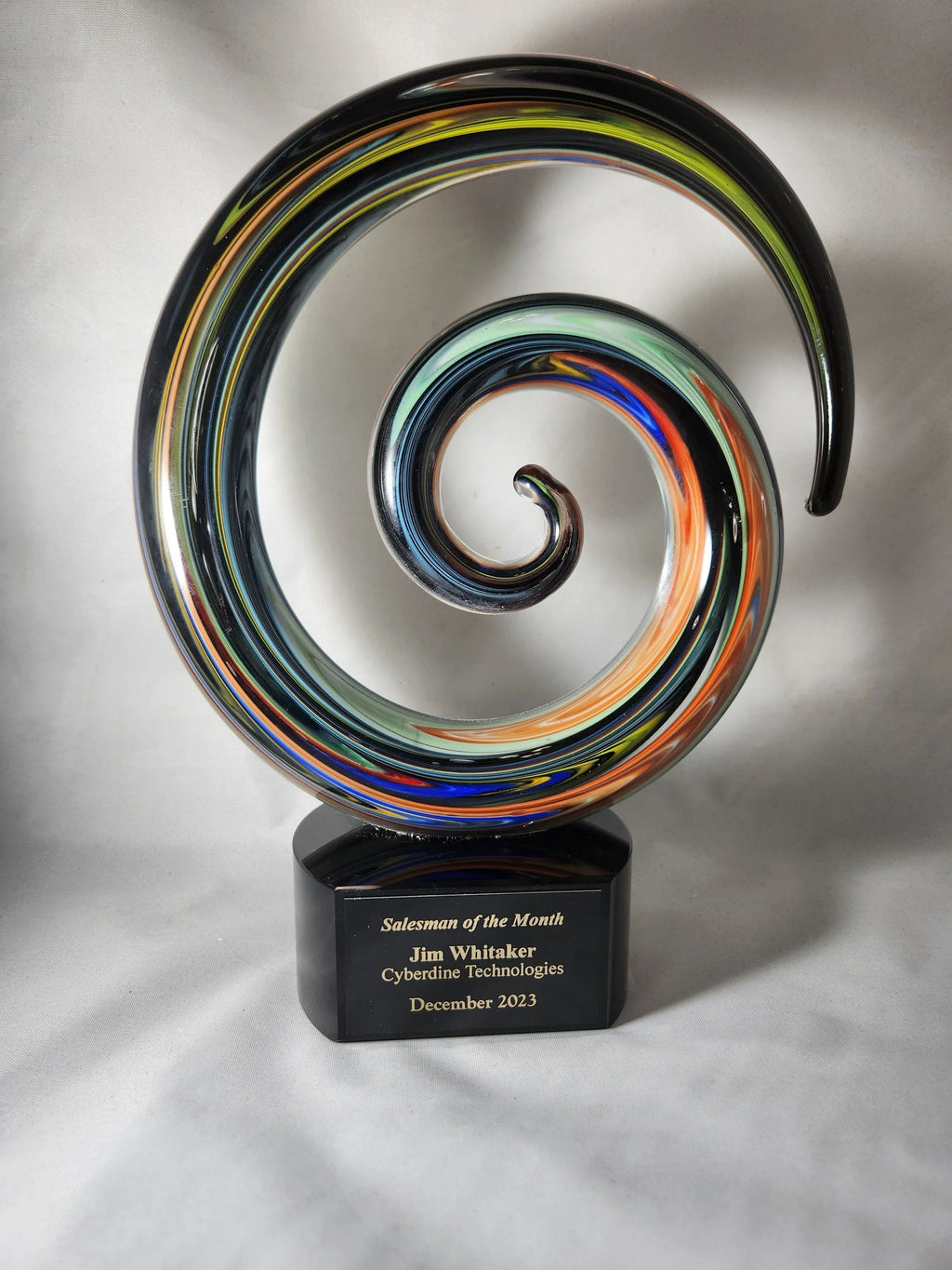 Colorful glass swirl award with engraved plaque for salesman of the month on white background