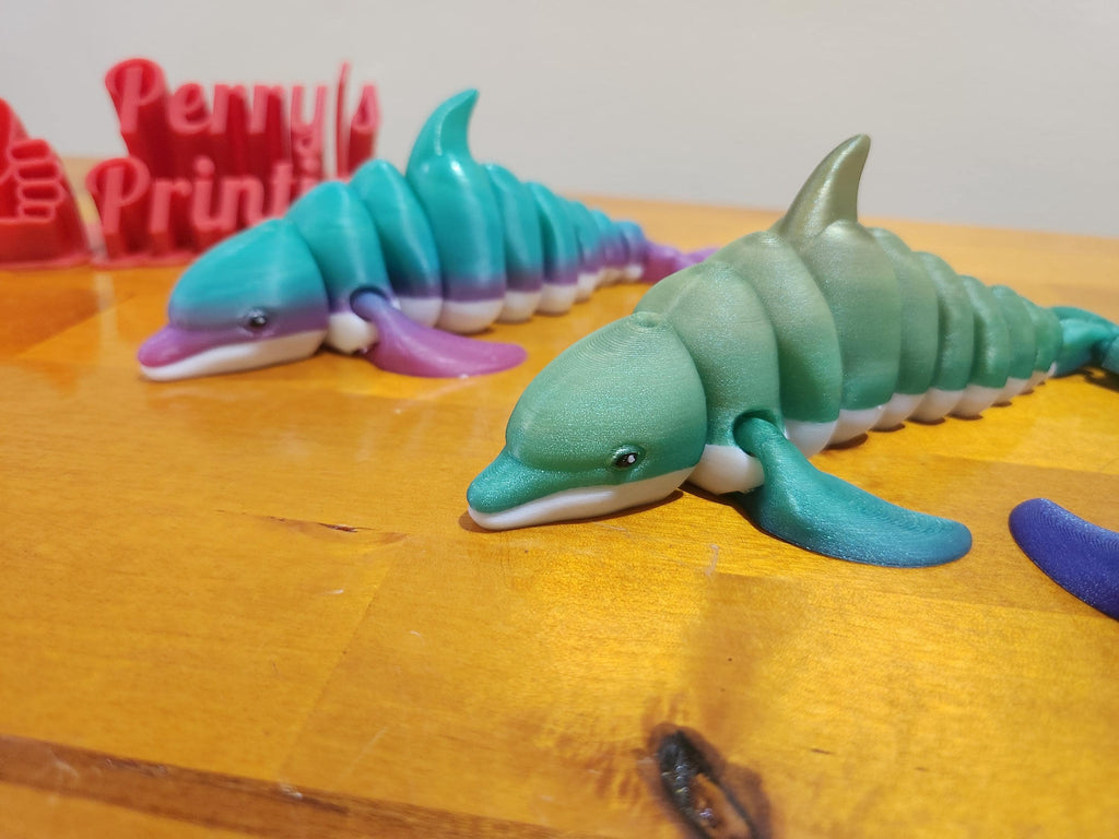 3D printed articulated dolphin shark toys in blue and purple on wood table