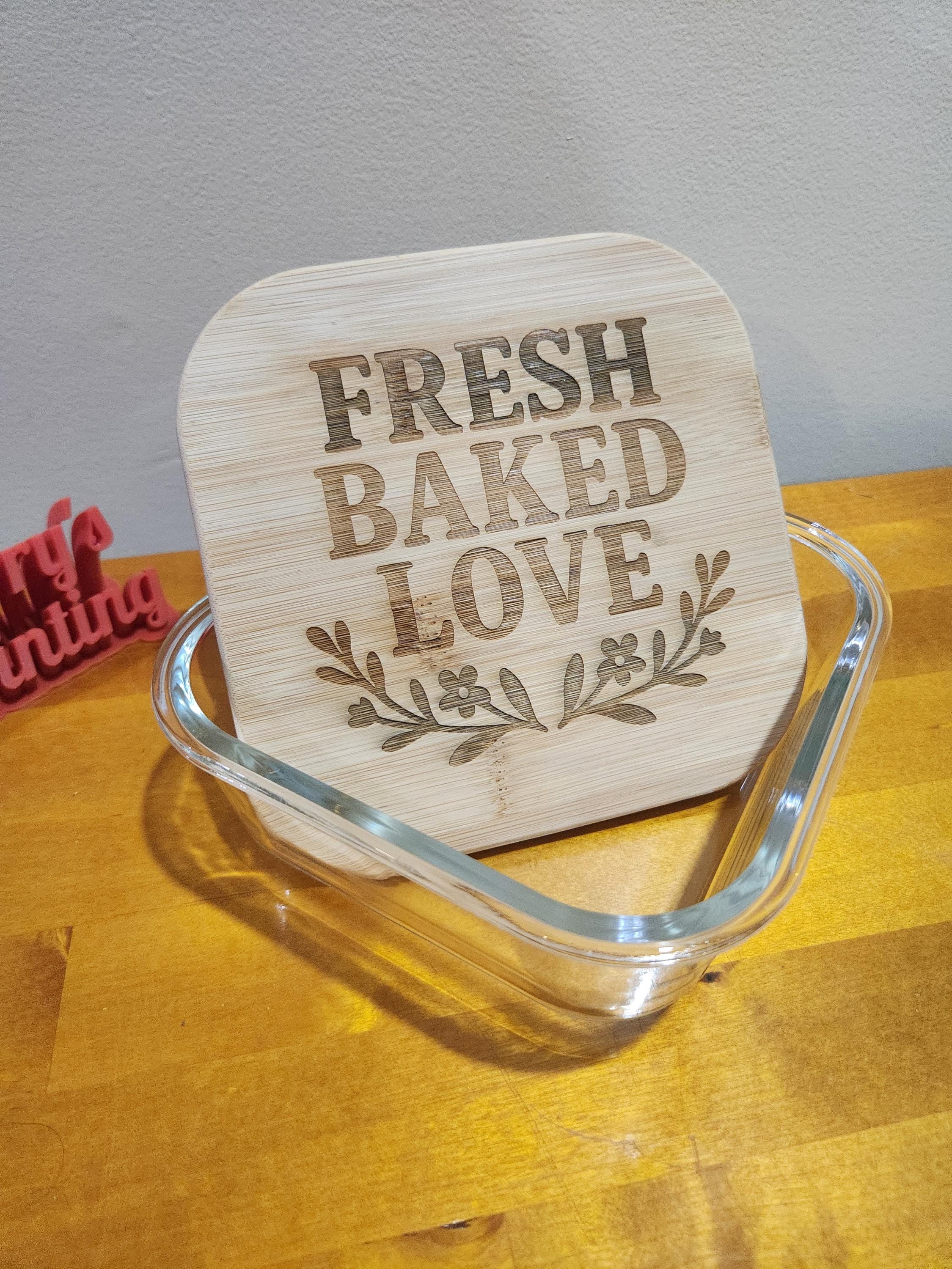 Laser engraved bamboo lid with 'Fresh Baked Love' on a glass baking dish, on wood table.