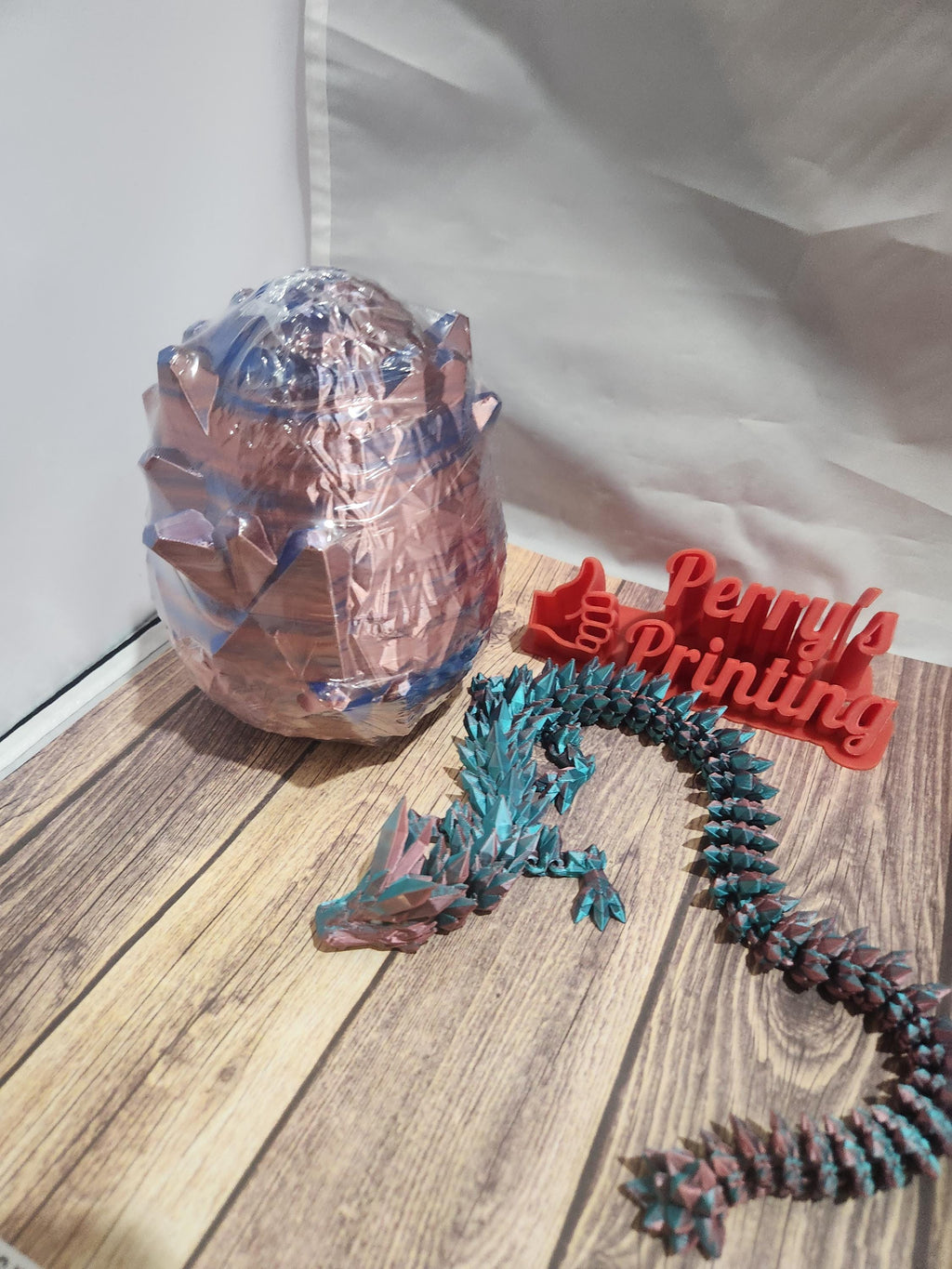 Colorful 3D printed dragon and dragon egg on wood surface, laser-cut Perry's Printing sign