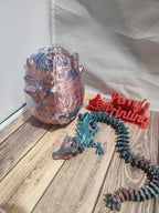 Colorful 3D printed dragon and dragon egg on wood surface, laser-cut Perry's Printing sign