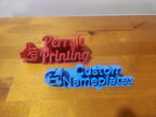 3D printed red and blue custom nameplates on a wooden surface
