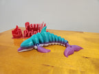 Colorful 3D printed articulated dolphin toy on wood table with red printed sign and thumbs up.