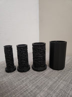 Four black 3D printed cylindrical objects, three with maze patterns, on a gray fabric surface.