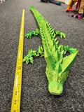 Large 3D printed green dragon with geometric design next to a measuring tape on carpet