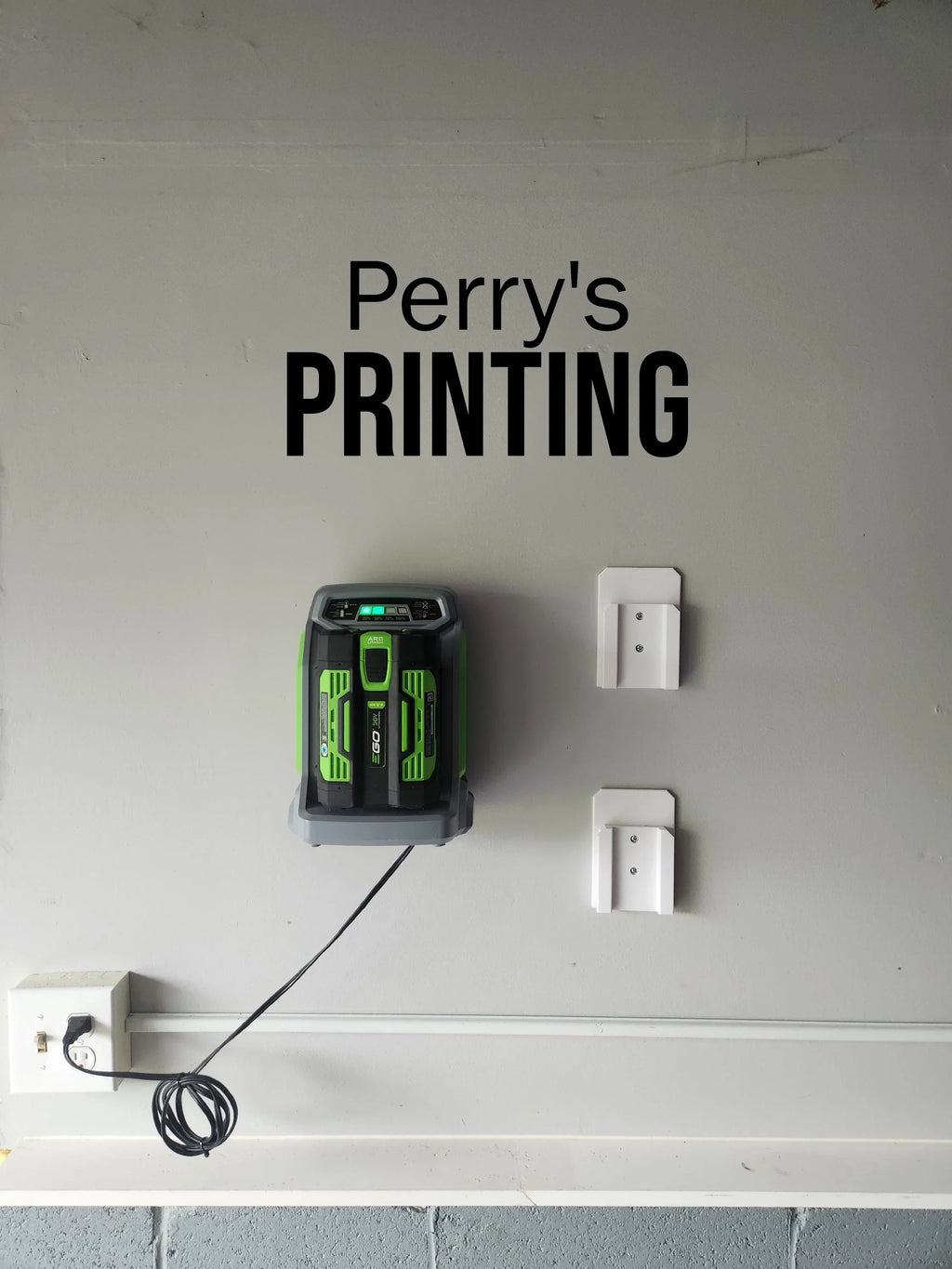 Wall-mounted battery charger and storage holders on gray wall, outlet with cord plugged in