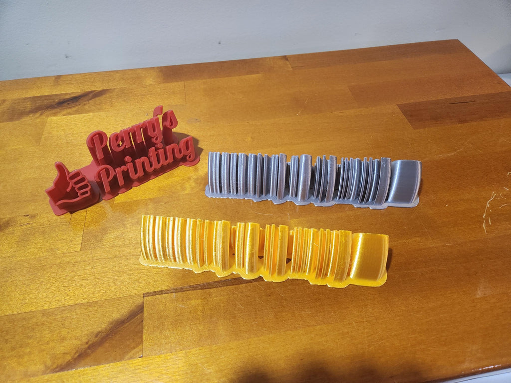 3D printed Perry's Printing sign with two filament sample swatches on wooden table