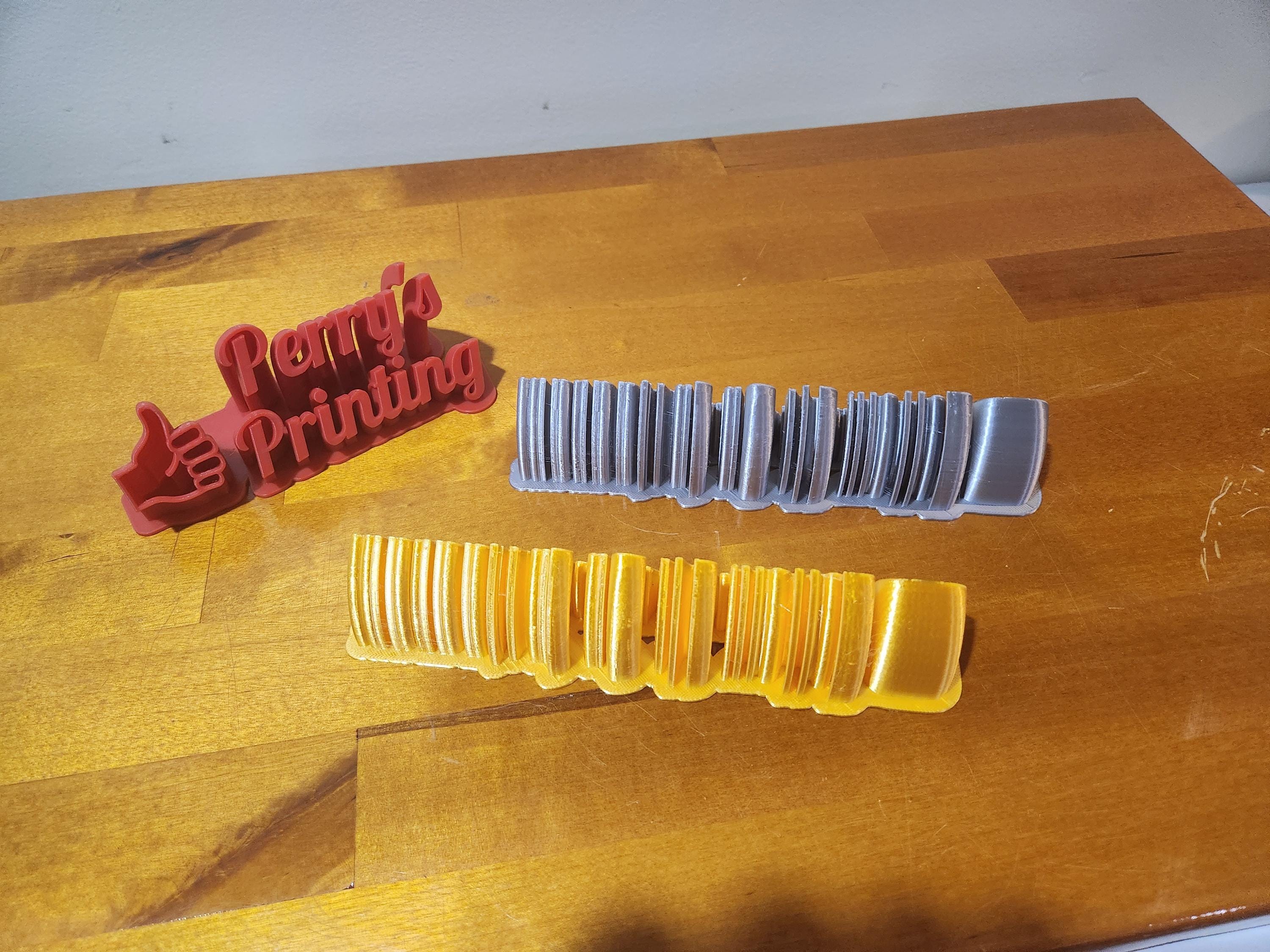 3D printed Perry's Printing sign with two filament sample swatches on wooden table