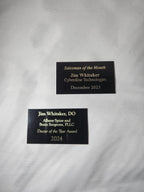 Two engraved black award plaques on white fabric, featuring custom text for recognition.