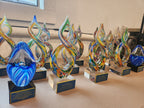 Colorful glass awards with engraved plaques lined up on a table for recognition ceremony