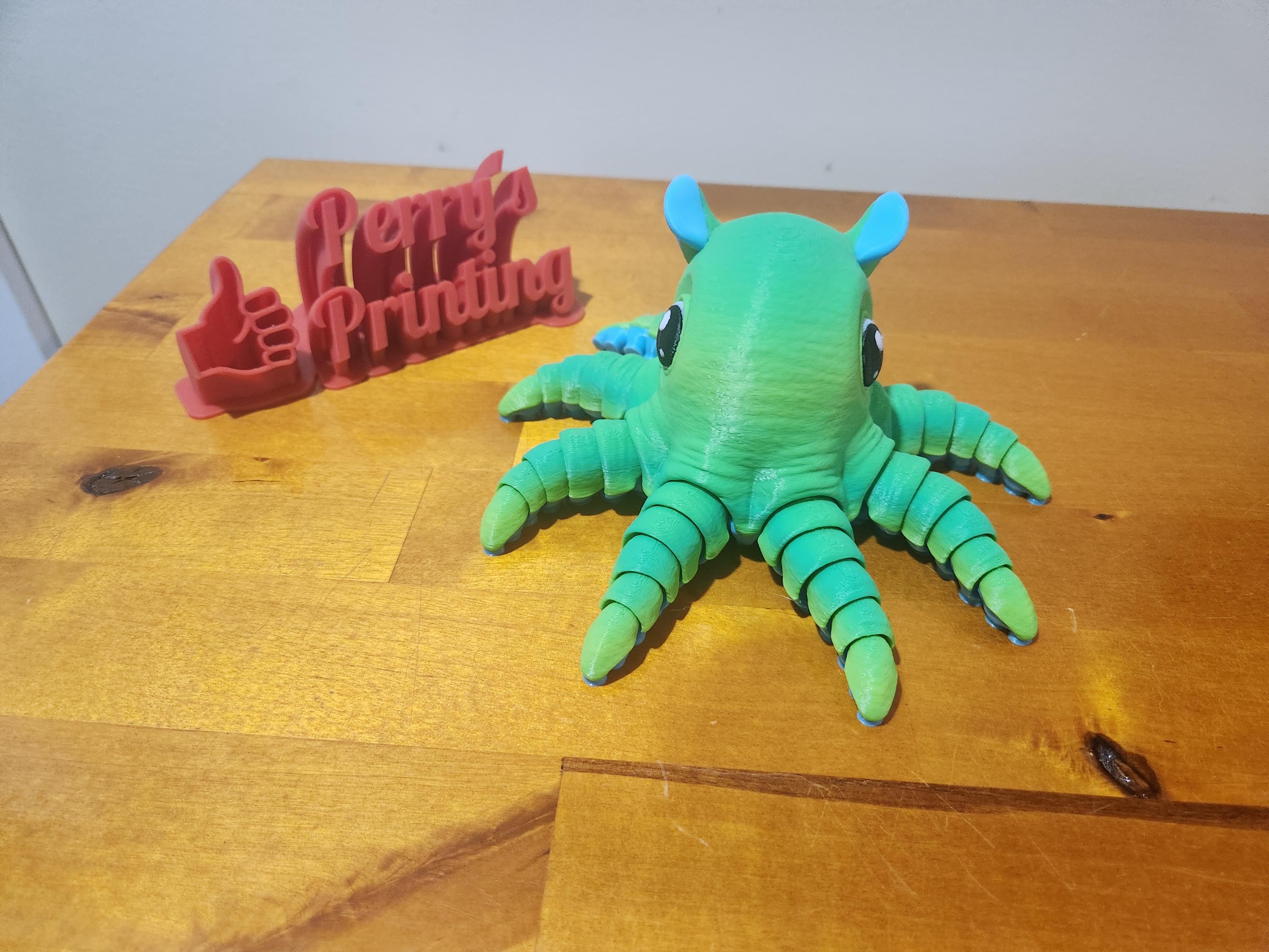 3D printed green octopus figure and red thumbs up sign on wood table