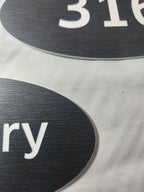 Close-up of custom black engraved signs with white text and brushed texture
