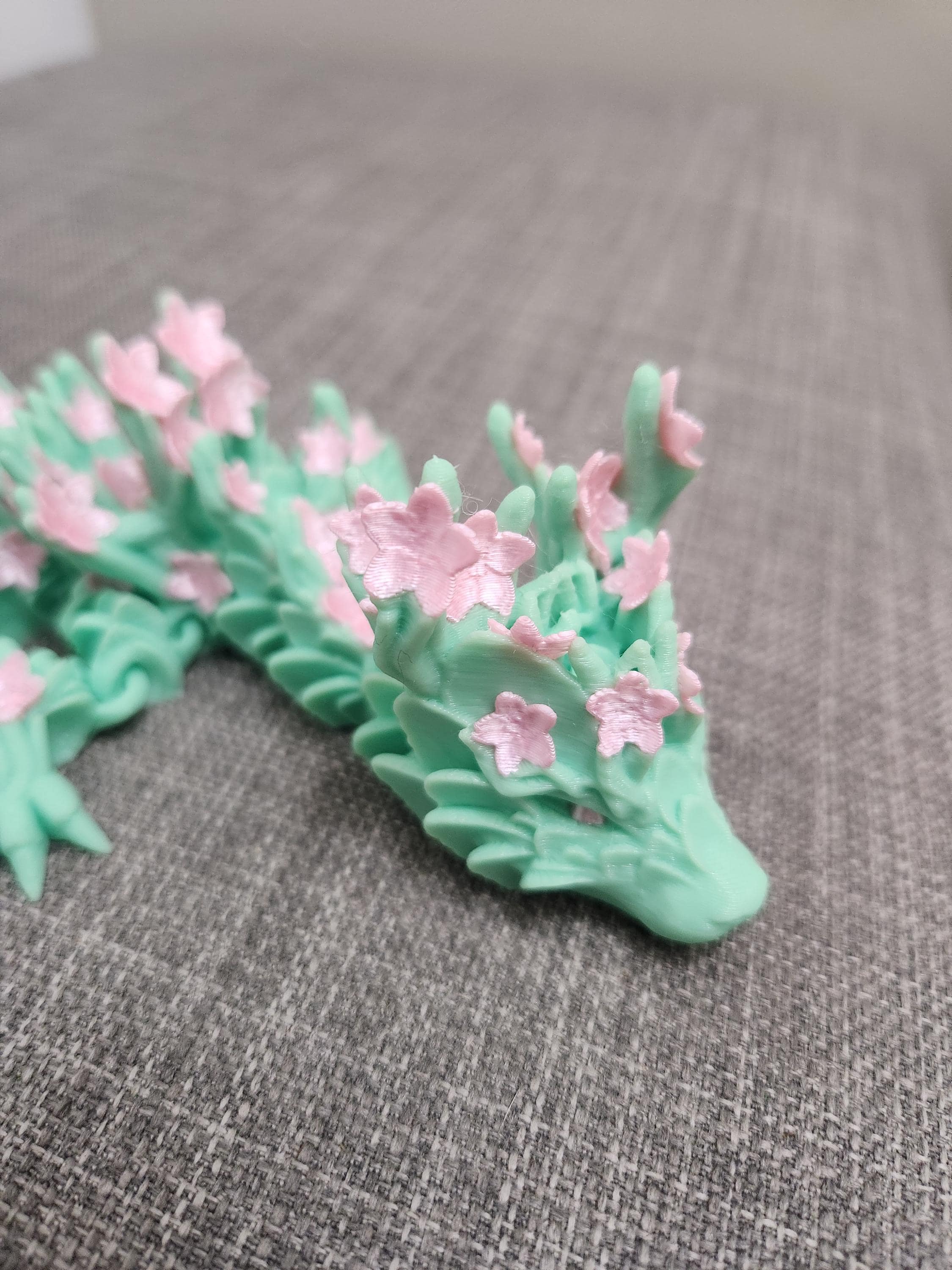 3D printed mint green dragon with pink cherry blossom flowers on textured gray fabric