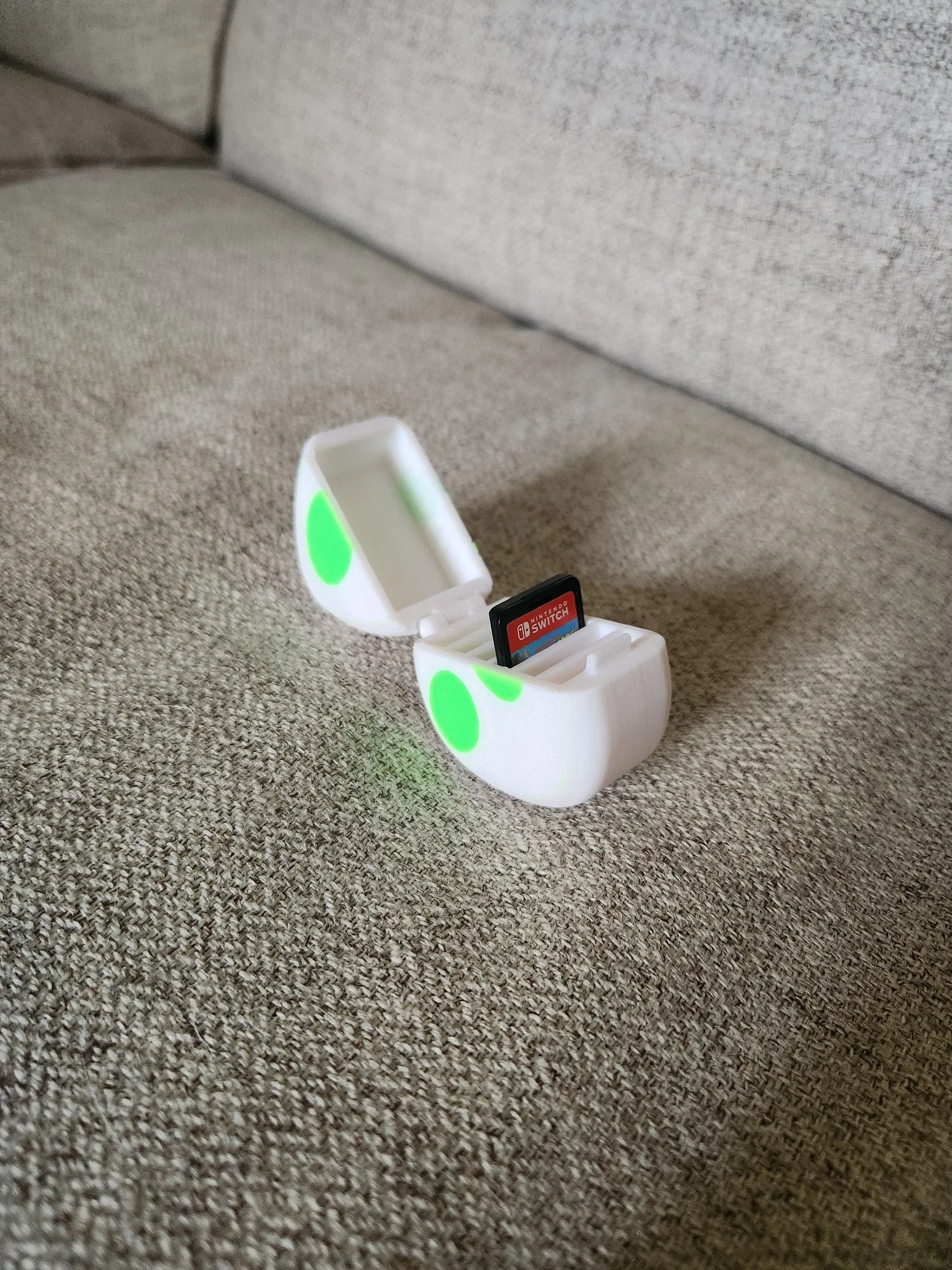3D printed white and green SD card case holding a Nintendo Switch game card on a beige couch