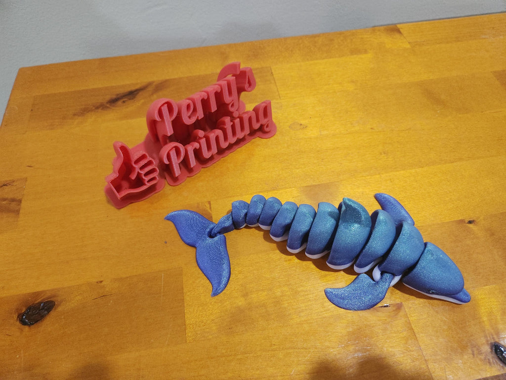 3D printed blue articulated whale and red sign on wooden table