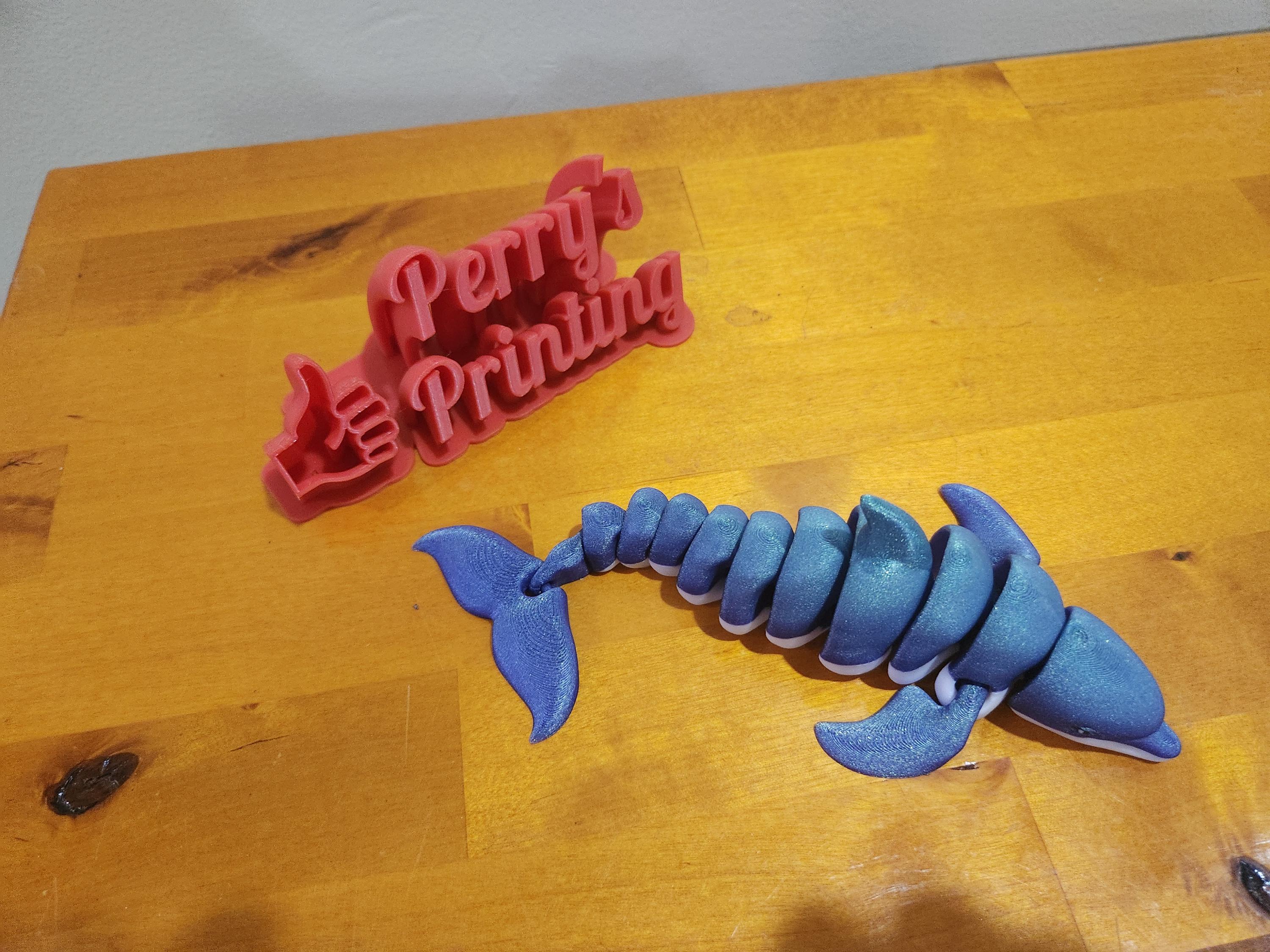 3D printed blue articulated whale and red sign on wooden table