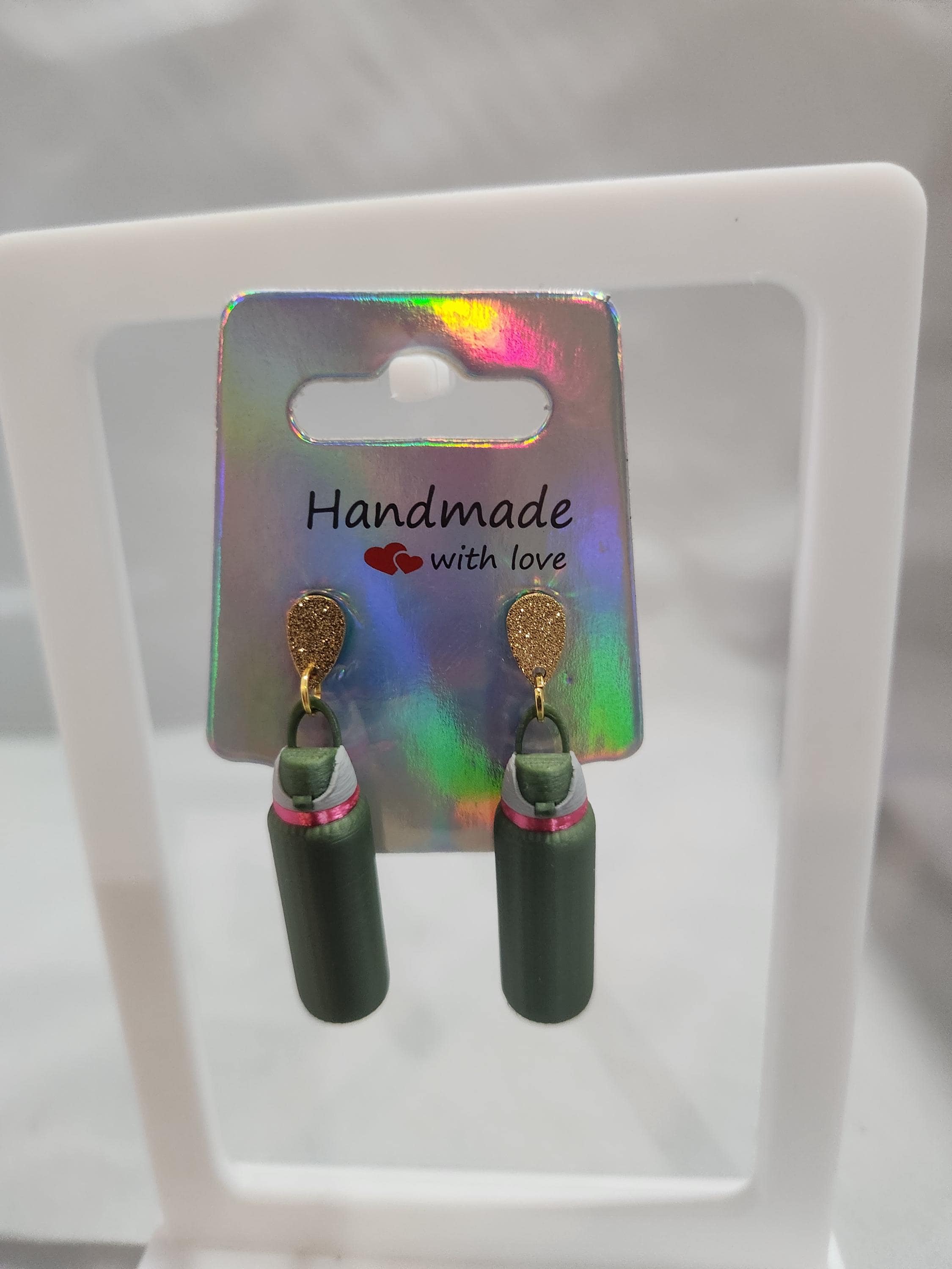 Handmade green and gold dangle earrings with pink accent, displayed on holographic card.