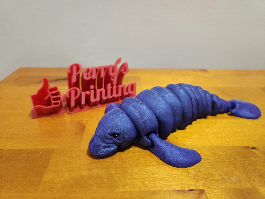 3D printed purple manatee figurine and red sign with thumbs up on wooden table