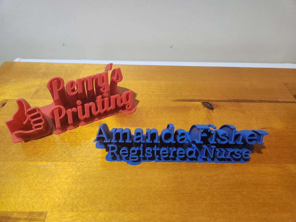 Custom 3D printed nameplates with engraved text on a wooden surface