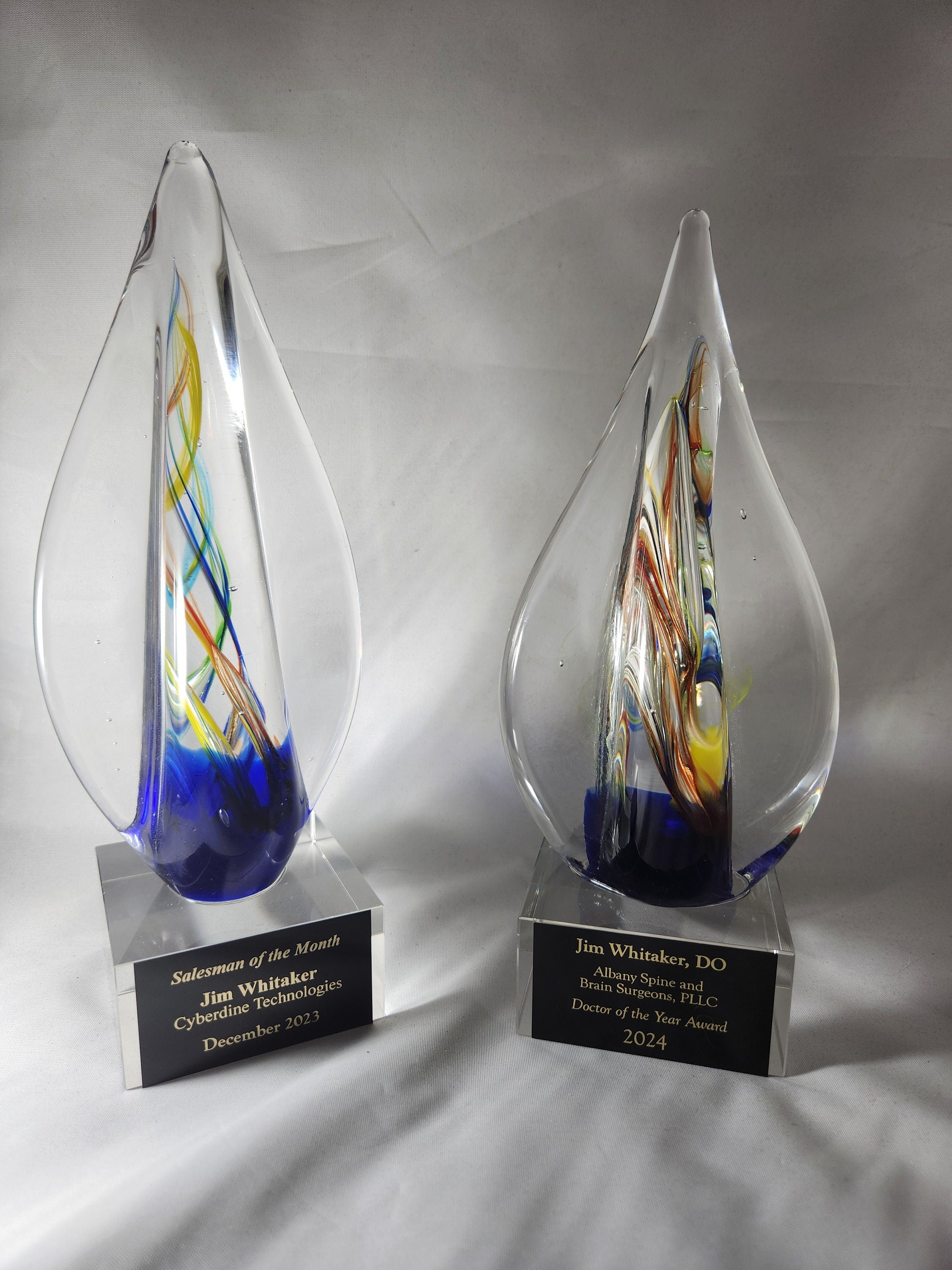 Two custom glass awards with colorful swirls and engraved bases for business recognition.