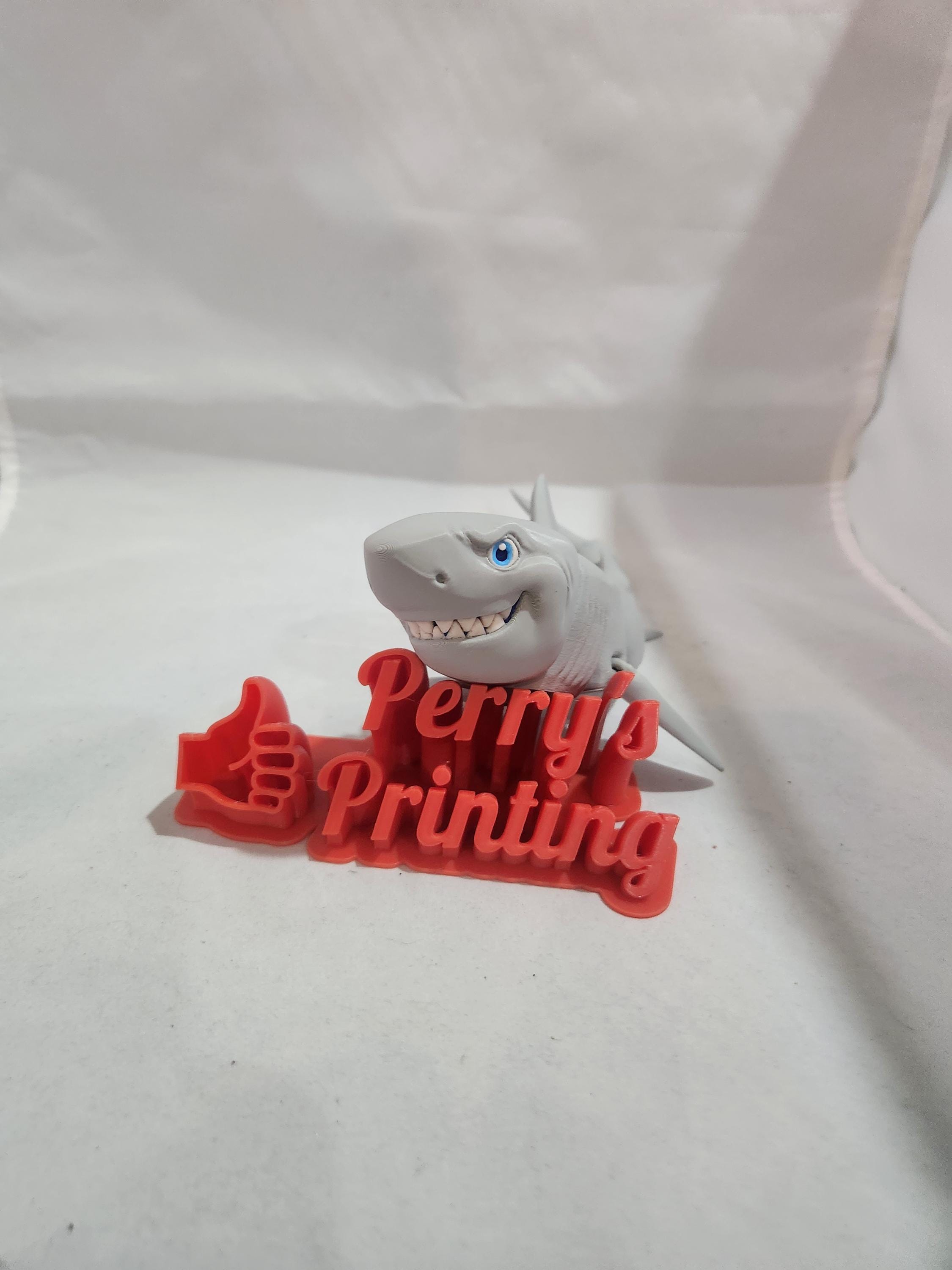 3D printed shark figure with red 'Perry's Printing' sign and thumbs-up symbol