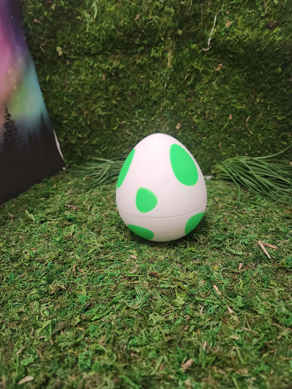 3D printed white egg with green spots on artificial grass background