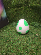 3D printed white egg with green spots on artificial grass background