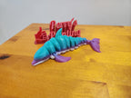 Colorful 3D printed articulated dolphin toy with red thumbs up sign on wooden table