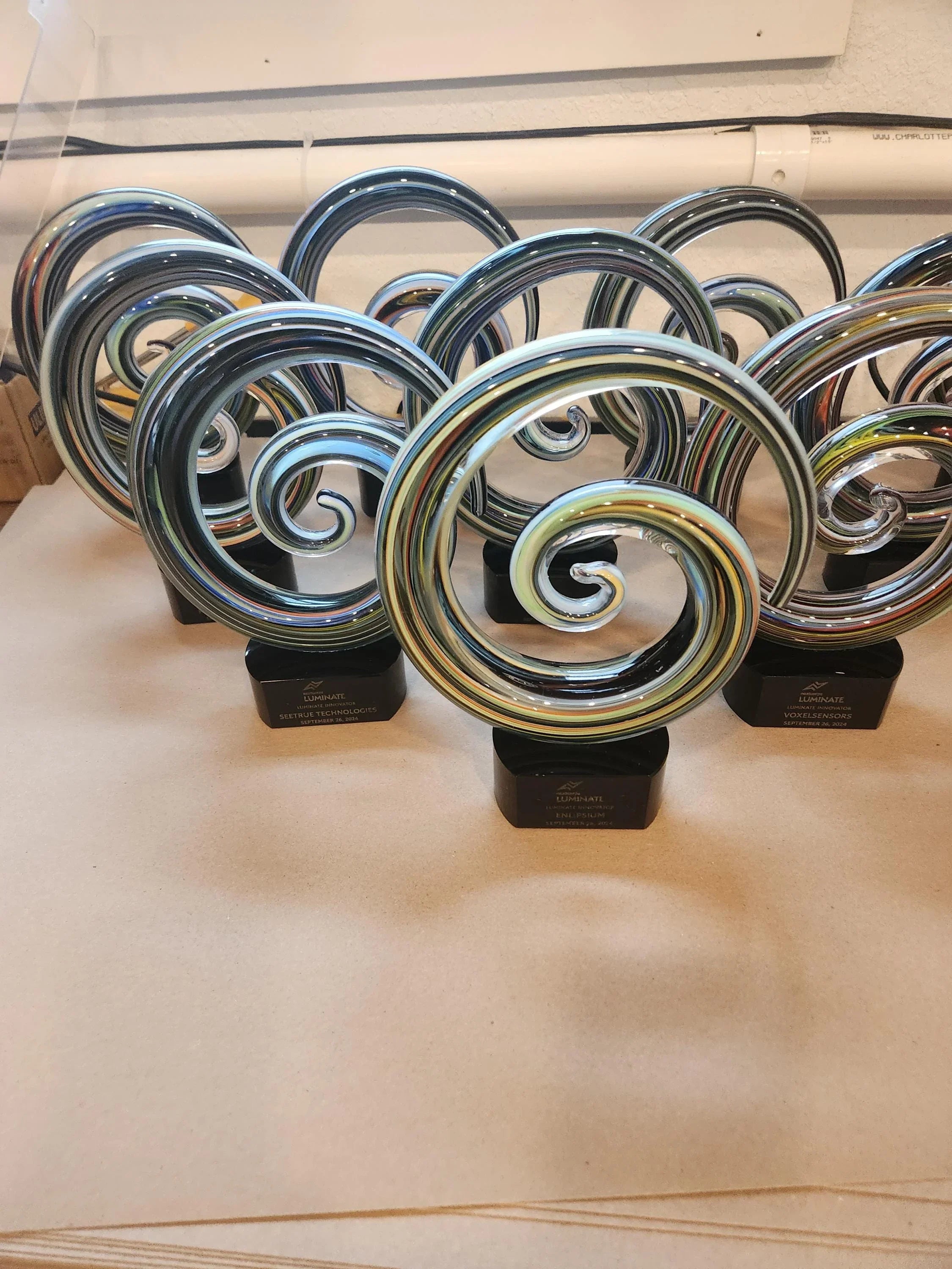 Colorful glass swirl awards with black bases displayed on a table, custom engraved trophies.