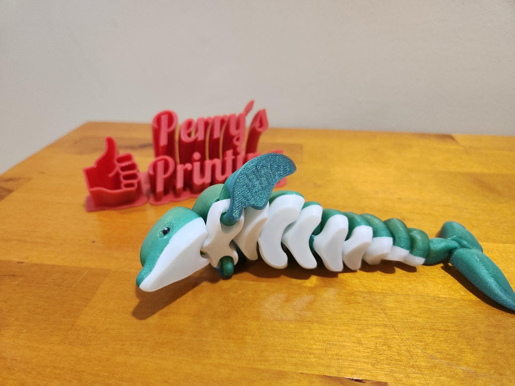 3D printed teal and white articulated dolphin figure with wings on wooden surface