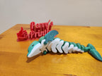 3D printed teal and white articulated dolphin figure with wings on wooden surface