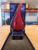 Glass teardrop award with red and black swirl design in gift box, custom engraved plaque
