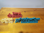 Colorful 3D printed custom signs with text and icons on a wooden surface