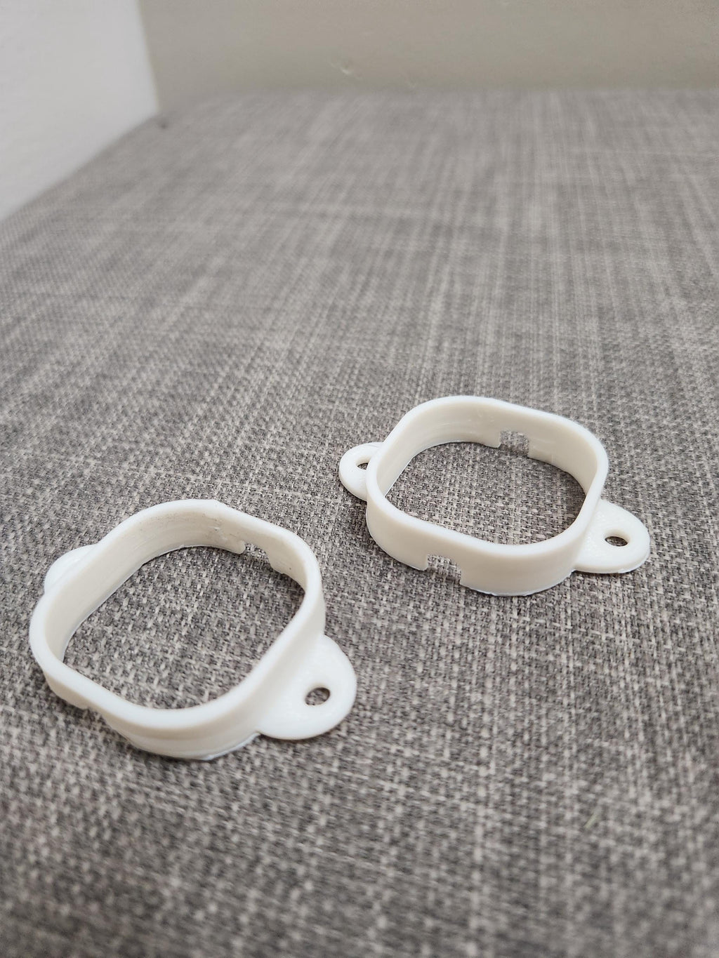 Two white 3D printed plastic mounting brackets on a gray textured surface