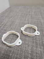 Two white 3D printed plastic mounting brackets on a gray textured surface