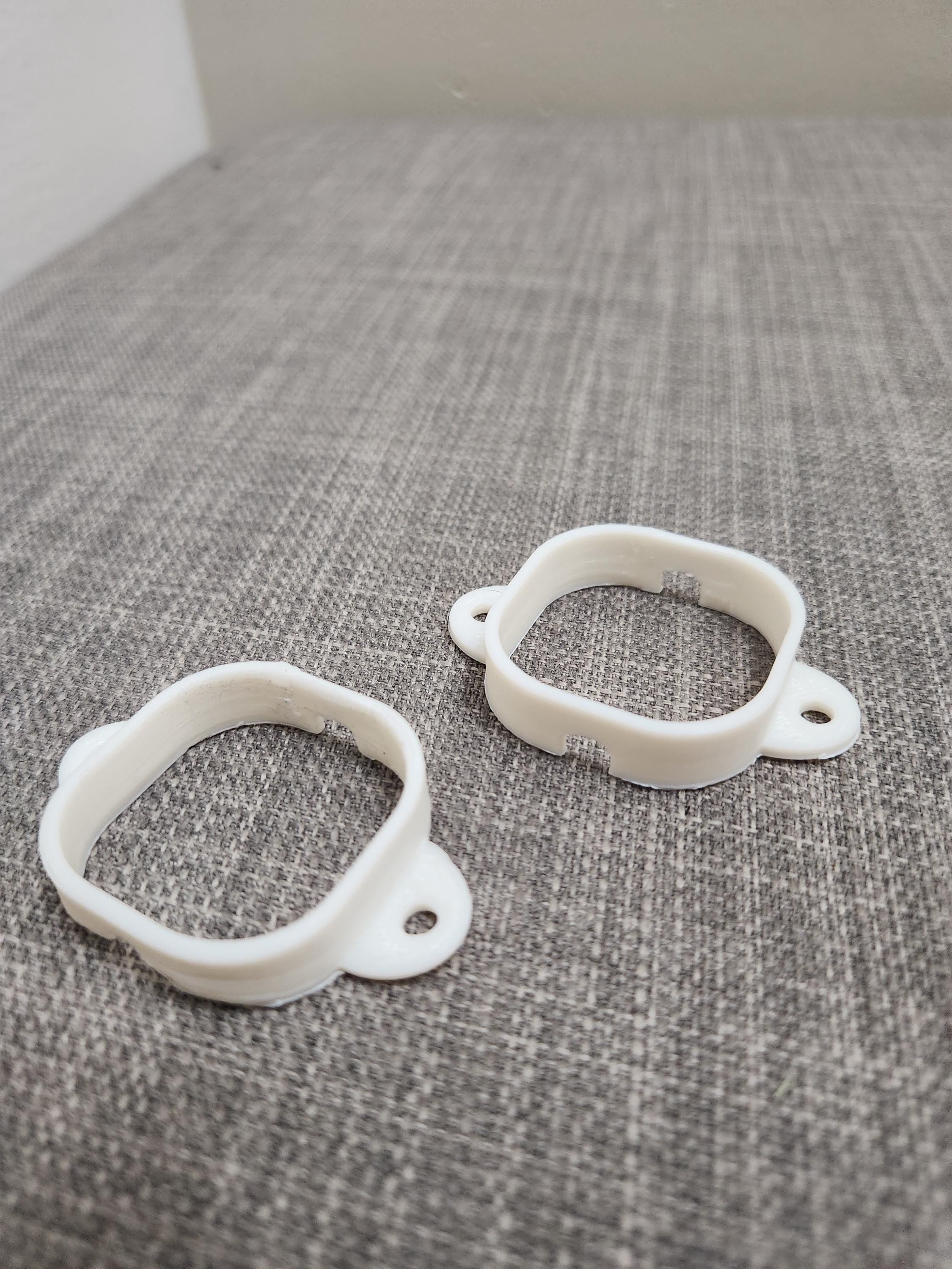 Two white 3D printed plastic mounting brackets on a gray textured surface