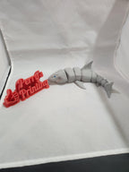 3D printed articulated shark figurine beside red 3D printed text on white background