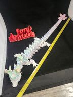 Pastel 3D printed articulated dragon measure with tape, floral accents, on black background