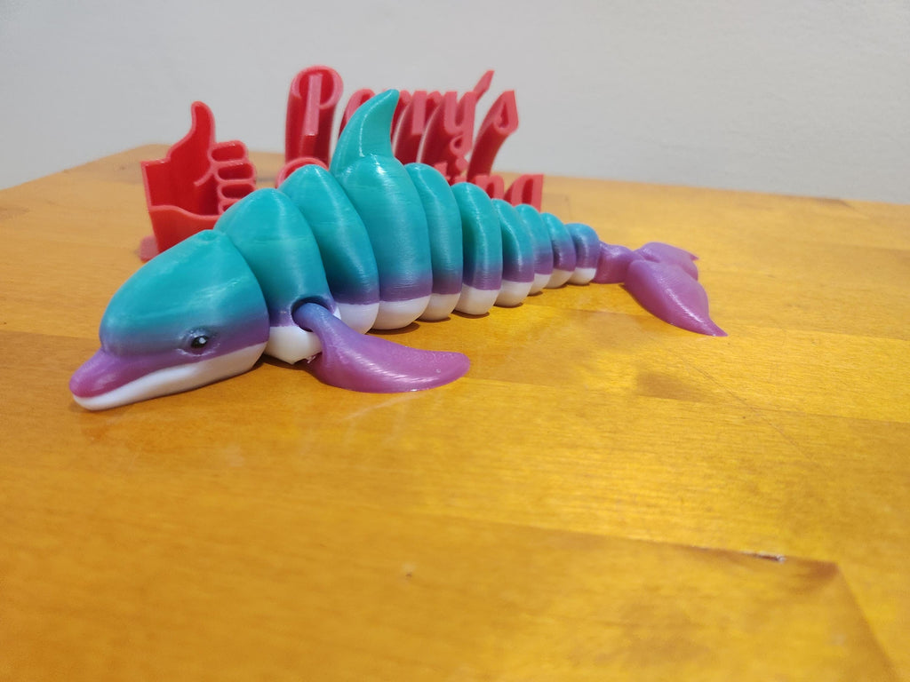 3D printed articulated dolphin toy in teal, purple, and white on wooden surface