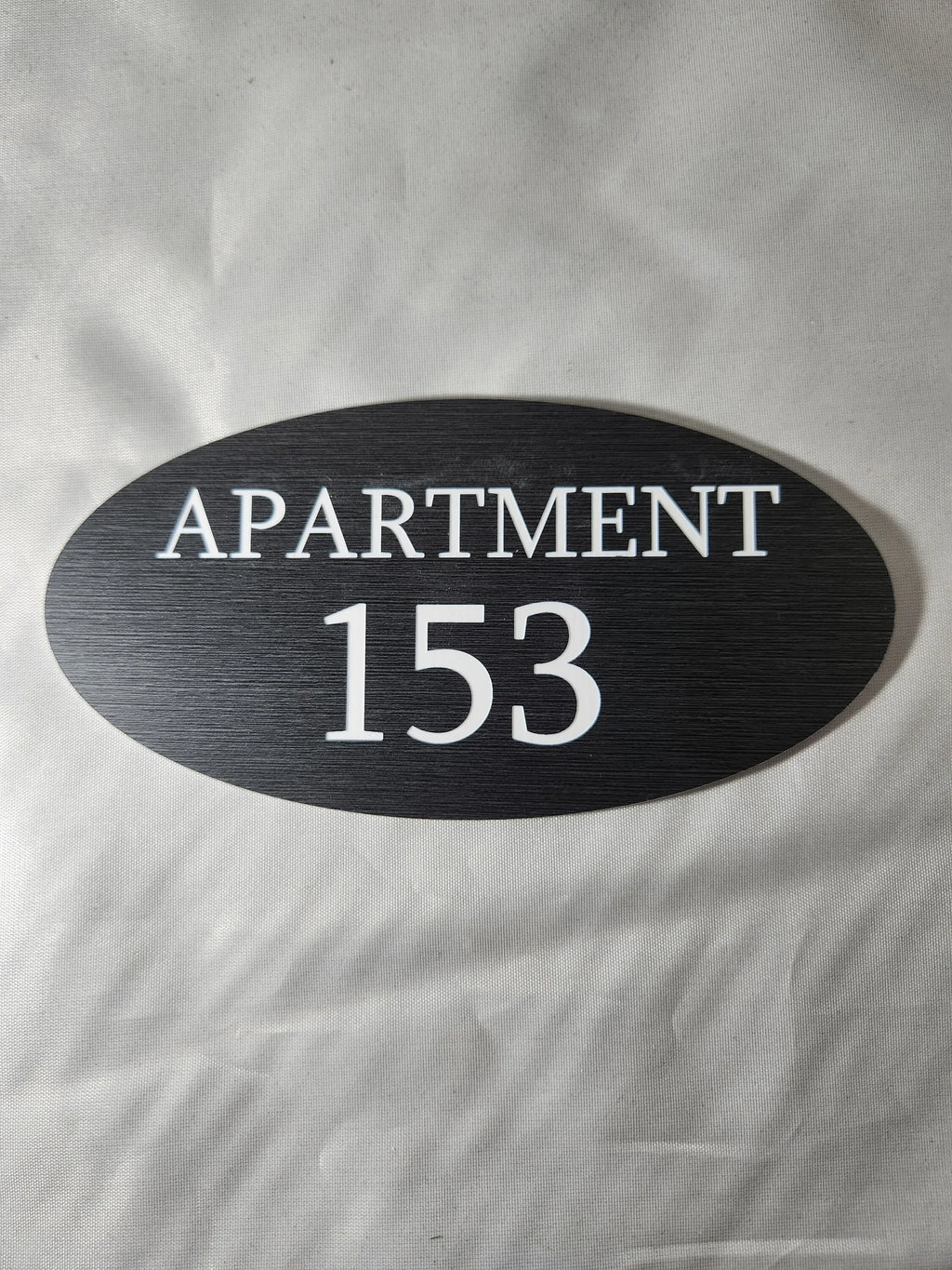 Custom oval black apartment number sign with white text reading 'Apartment 153'